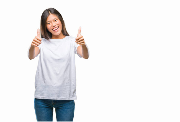 Young asian woman over isolated background approving doing positive gesture with hand, thumbs up smiling and happy for success. Looking at the camera, winner gesture. - Foto, Imagen