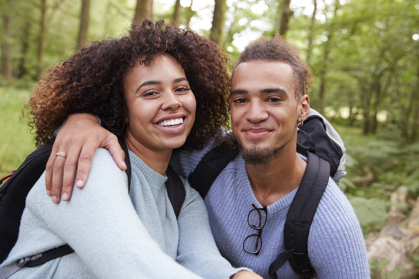 Young mixed race couple smiling to camera during a hike in a forest, close up portrait - Foto, afbeelding