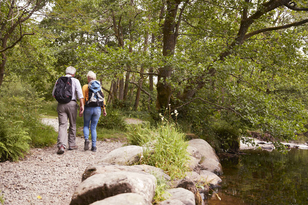 Rear View Of Senior Couple Hiking Along Path By River In UK Lake District - Foto, immagini