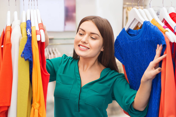gelukkig vrouw kiezen kleding in kleding winkel - Foto, afbeelding