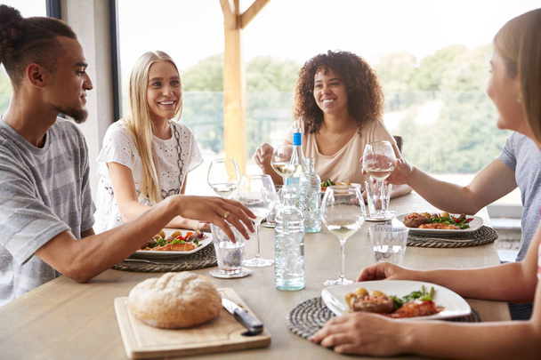 Multi ethnic group of five young adult friends eating, drinking,  talking and smiling during a dinner party - Foto, afbeelding