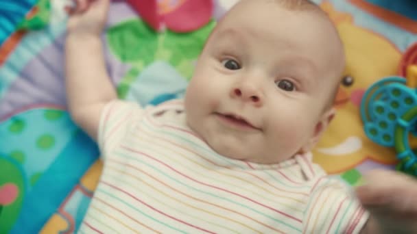 Muotokuva pikkulapsesta katsomassa kameraa värillisellä matolla. Lähikuva söpö vauva kasvot
 - Materiaali, video