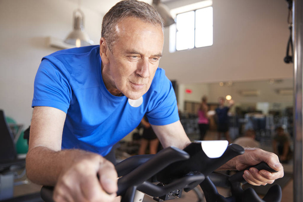 Senior Man Exercising On Cycling Machine In Gym - Foto, afbeelding
