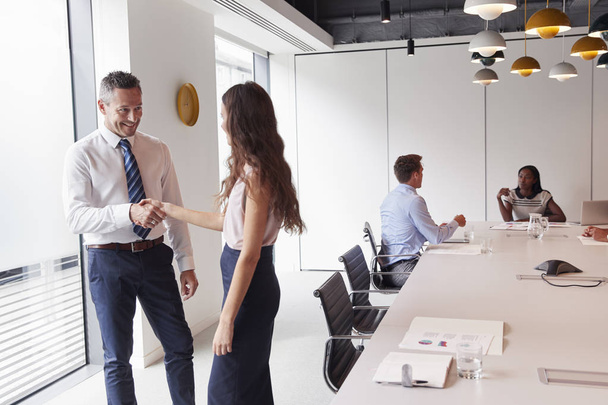 Businessman And Businesswoman Shaking Hands In Modern Boardroom With Colleagues Meeting Around Table In Background - Foto, afbeelding
