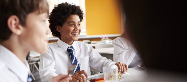 Група старшокласників носять уніформу сидячи навколо столу і їдять обід в Кафетерії
  - Фото, зображення