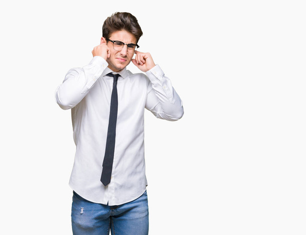 Young business man wearing glasses over isolated background covering ears with fingers with annoyed expression for the noise of loud music. Deaf concept. - Photo, Image