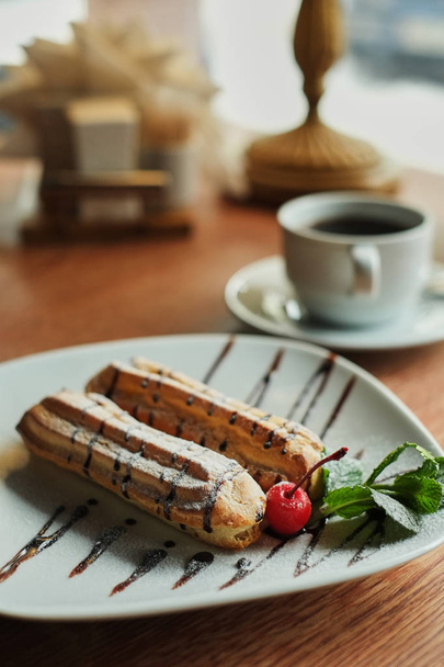 Two sweet french eclairs on plate. Breakfast in cafe. wooden table background side view - Foto, Imagen