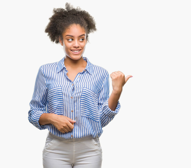 Młody afro american kobieta na białym tle uśmiechnięty z szczęśliwy twarz patrząc i skierowaną do boku z kciukiem w górę. - Zdjęcie, obraz