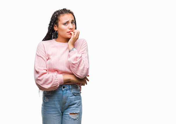 Молодая косичка африканская американка в свитере на изолированном фоне выглядит напряженной и нервной с руками во рту, грызущими ногти. Проблема тревоги
. - Фото, изображение