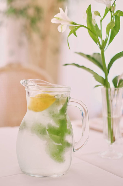 Glass jug of cold lemonade on a light background cafe. Pitcher lemon water with mint. - Foto, Imagen