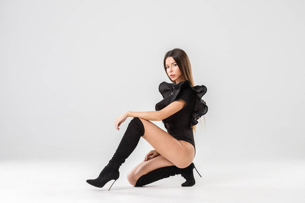 Fashion studio portrait of beautiful female model in black clothes. Young brunette woman with long hair sitting on white background - Zdjęcie, obraz