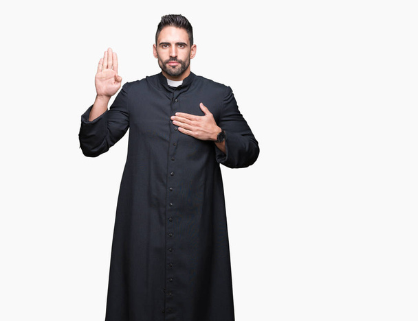 Jovem padre cristão sobre fundo isolado Jurando com a mão no peito e palma aberta, fazendo uma promessa de lealdade juramento
 - Foto, Imagem