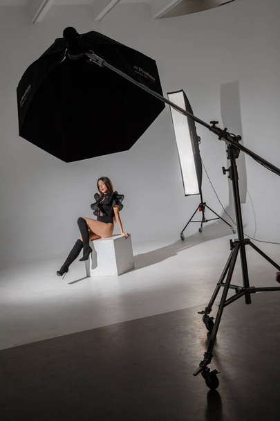 Fashion studio portrait of beautiful female model in black clothes. Young brunette woman with long hair sitting on white background - Fotografie, Obrázek
