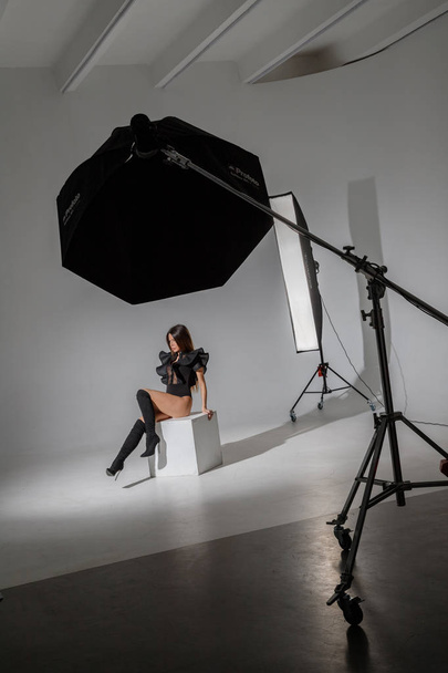Fashion studio portrait of beautiful female model in black clothes. Young brunette woman with long hair sitting on white background - Foto, afbeelding