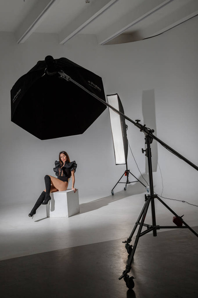 Fashion studio portrait of beautiful female model in black clothes. Young brunette woman with long hair sitting on white background - Fotó, kép