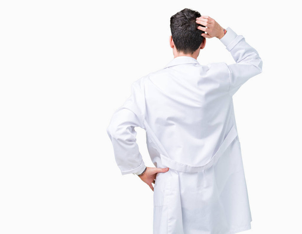 Jonge professionele wetenschapper-man dragen witte vacht over geïsoleerde achtergrond terug denken over twijfel met hand op hoofd - Foto, afbeelding