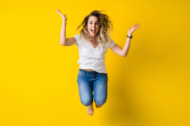 Beautiful young blonde woman jumping happy and excited over isolated yellow background - Photo, Image