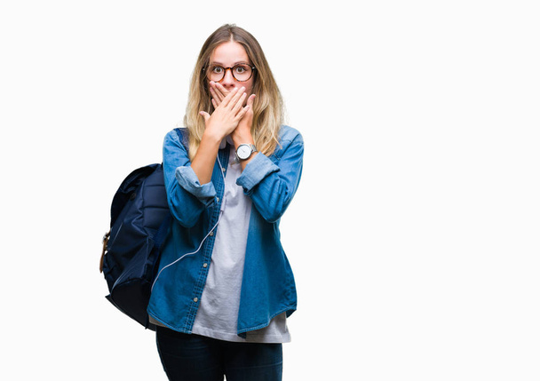 Young beautiful blonde student woman wearing headphones and glasses over isolated background shocked covering mouth with hands for mistake. Secret concept. - Photo, Image