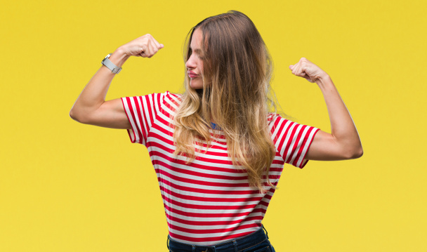 Young beautiful blonde woman over isolated background showing arms muscles smiling proud. Fitness concept. - Photo, Image