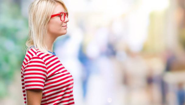Mladá krásná blondýna žena nosí brýle izolované pozadí pohledu na stranu, uvolnit profilu pozice s přirozenou tvář s sebejistý úsměv. - Fotografie, Obrázek