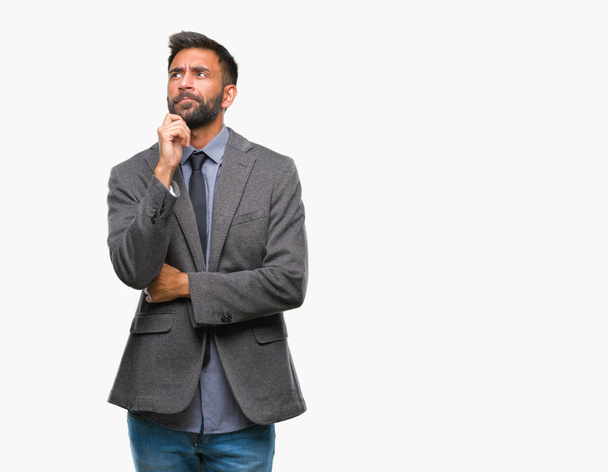 Adult hispanic business man over isolated background with hand on chin thinking about question, pensive expression. Smiling with thoughtful face. Doubt concept. - Photo, image
