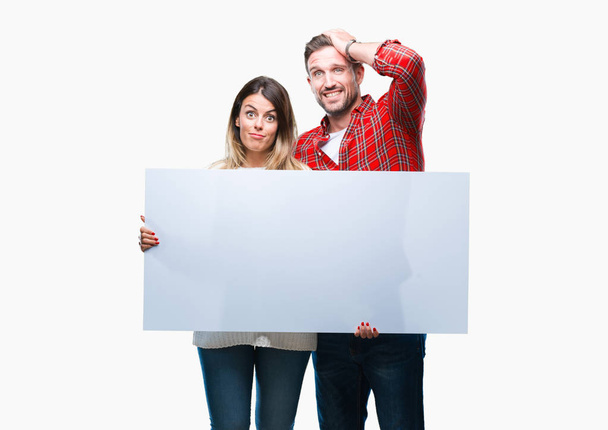 Young couple together holding blank banner over isolated background stressed with hand on head, shocked with shame and surprise face, angry and frustrated. Fear and upset for mistake. - Photo, Image