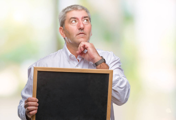 schöner älterer Lehrer Mann hält Tafel über isoliertem Hintergrund ernstes Gesicht über Frage nachdenkend, sehr verwirrte Idee - Foto, Bild