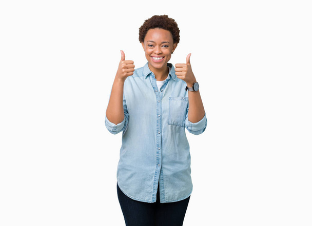 Молодая красивая африканская американка на изолированном фоне знак успеха делает позитивный жест с рукой, большие пальцы вверх улыбается и счастлив. Глядя в камеру с веселым выражением лица, жест победителя
. - Фото, изображение
