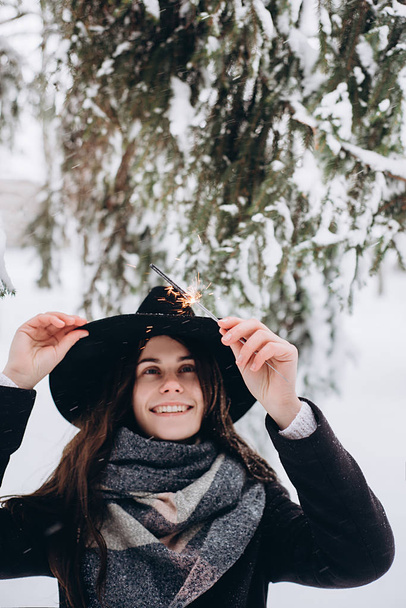 Happy and smiling girl in a hat keeps Bengal lights on the street during snowfall. Winter concept - Fotó, kép
