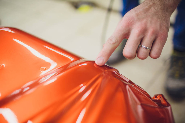 Car wrapping specialist putting vinyl foil or film car wrapping protective film yacht, boat, ship, car, mobile home. orange film heating with hair dryer and trimming plastic soft hard squeegee - 写真・画像
