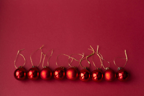 Red Christmas tree decorative toy balls on red celebratory Christmas background laid out in horizontal line. New Year's holidays. Christmas holidays. - 写真・画像