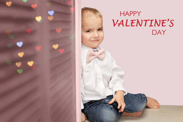 Niño en camisa blanca y suave pajarita rosa sentado en el escritorio y mirando con confianza, se enamora, concepto romántico y amor, saludo de San Valentín
 - Foto, Imagen