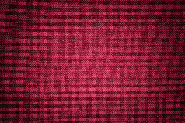 Dark red background from a textile material with wicker pattern, closeup. Structure of the wine fabric with texture. Cloth maroon backdrop with vignette. - Photo, Image