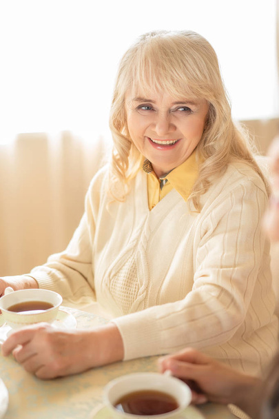 Vertical portrait of smiling elderly woman sitting at table - Foto, Imagen