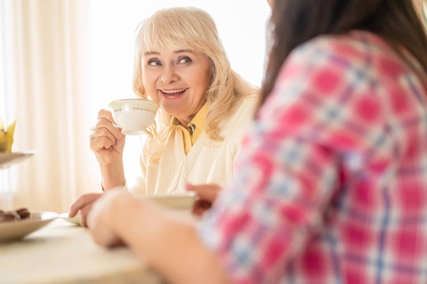 Smiling woman drinks tea and enjoys conversation with a daughter - Foto, Imagen
