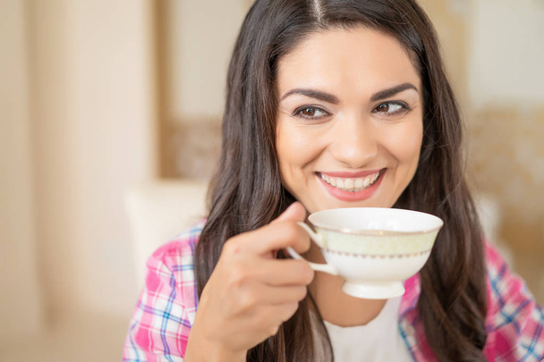 Smiling beautiful brunette drinks a cup of tea. - Zdjęcie, obraz