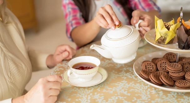 Hands of young woman with white china teapot pouring tea into cup of her senior mother - Foto, Imagem