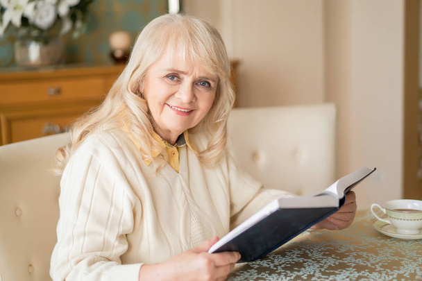 Elegant senior woman reads book at table and having tea - Foto, Imagen