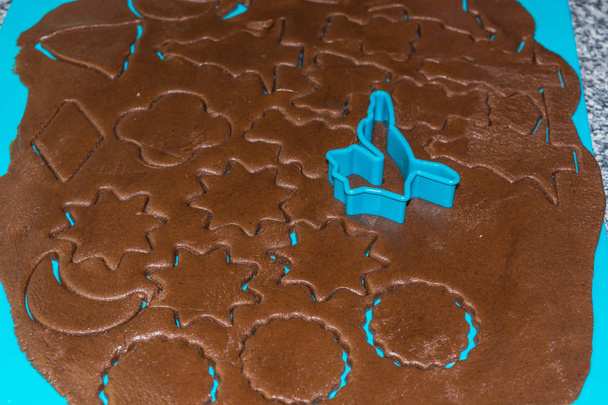 A nyers tésztát kiütik az ünnepi sütikért egy kék alátéten. Mézeskalács sütit készítek. Lépések a keksz készítéshez. Felülnézet. - Fotó, kép