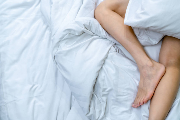 Κοντινό πλάνο γυμνά πόδια γυναίκα στο κρεβάτι, πάνω από το λευκό φύλλο κουβέρτα και κρεβάτι στην κρεβατοκάμαρα του σπιτιού ή του ξενοδοχείου. Στον ύπνο και να χαλαρώσετε έννοια. Τεμπέλης πρωί. Ξυπόλυτος γυναίκα ξαπλωμένη στο κρεβάτι λευκό άνεσης και Παπλωματοθήκες. - Φωτογραφία, εικόνα