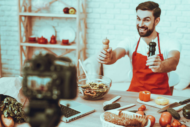 Blogger Makes a Video. Blogger is Smiling Beard Man. Video About a Cooking. Camera Shoots a Video. Laptop and Different Food on Table. Man Showing a Seasonings. Man in Studio Interior. - Zdjęcie, obraz