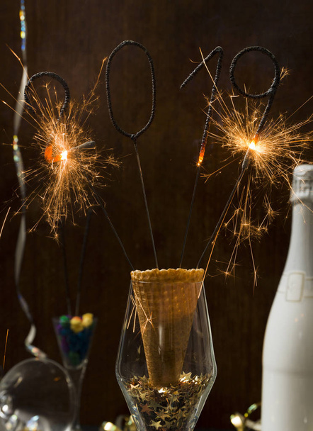 new year background with burning sparklers in glass and champagne bottle with Christmas items on background   - Fotografie, Obrázek