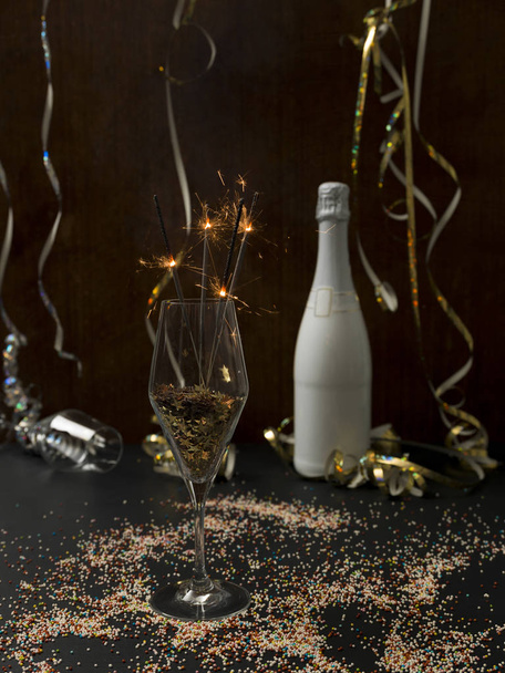 Новый год фон с горящими бенгальскими огнями в стекле и бутылка шампанского с рождественскими предметами на заднем плане
   - Фото, изображение