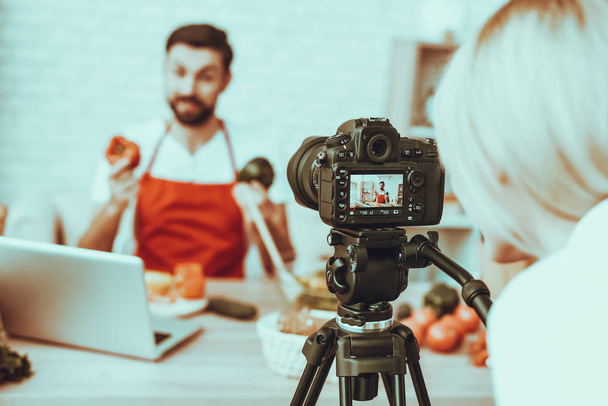 Blogger Makes a Video. Blur View of Blogger. Video About a Cooking. Woman Operator Shoots a Video on Camera. Different Food on Table. Man Showing a Peppers. People in Studio Interior. - Фото, изображение
