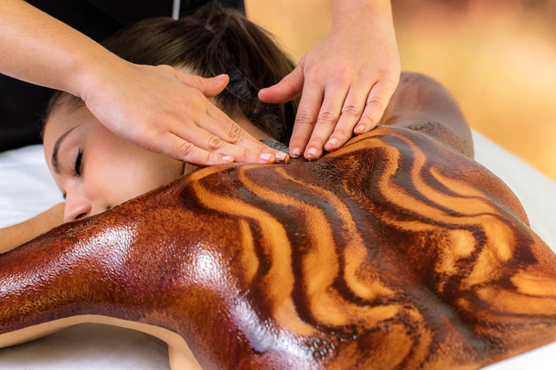 Primo piano di donna che ha caldo antiossidanti cioccolato massaggio alla schiena. Estetista sfregamento cera di cacao scuro sulla pelle
. - Foto, immagini