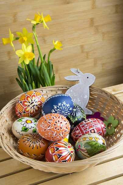 Domácí ručně malovaná vajíčka a dřevěný zajíček v koši, žlutý Narcis žlutý květ, dřevěné pozadí, Velikonoční dekorace na stůl - Fotografie, Obrázek