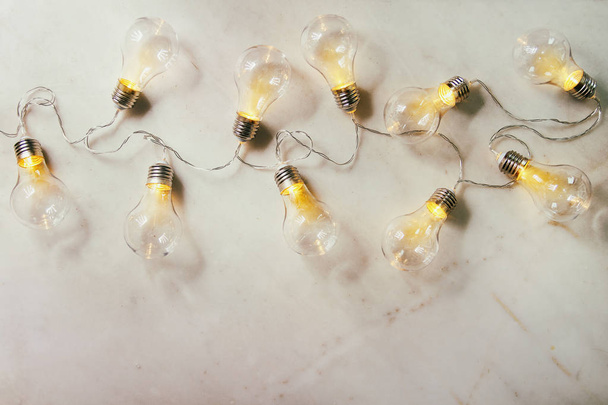 Retro christmas garland with lighted lamps over white marble background. Flat lay, space - 写真・画像