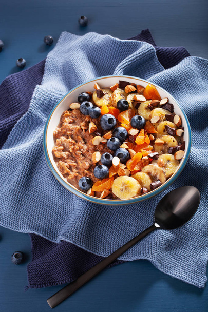 chocolade havermoutpap met bosbes, noten, bananen, gedroogde abrikoos voor gezond ontbijt - Foto, afbeelding
