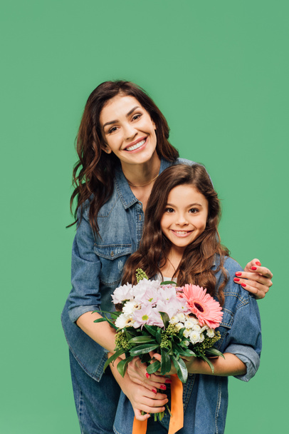smiling mother embracing daughter with flower bouquet isolated on green - Foto, Imagem