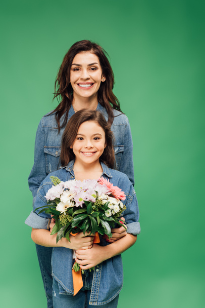 mother and daughter looking at camera and holding flower bouquet isolated on green - Foto, Imagen